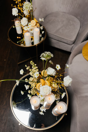 A composition of candles, flowers, and lemons on small tables with armchairs in the backgroundの写真素材