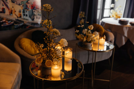 A composition of candles, flowers, and lemons on small tables with armchairs in the background, set in a modern interior. Home decor.の写真素材