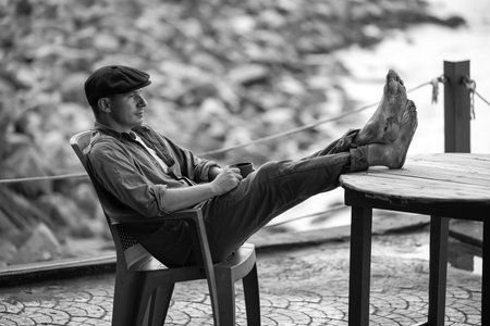 An attractive man has put his feet on the table. He is sitting in a relaxed position on the beach,...