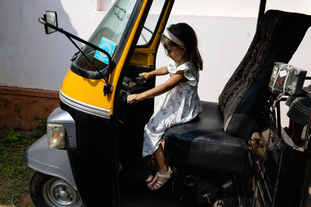 Caucasian girl with dark hair in a white dress poses behind the wheel of an Indian motorized...