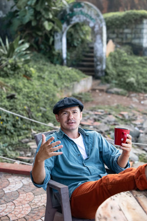 The man wearing a hat is talking while sipping coffee from a red mugの写真素材