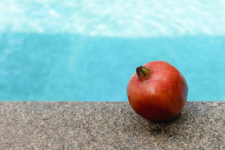 A beautiful red pomegranate lies against the backdrop of a swimming pool.の写真素材
