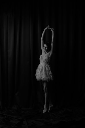 Fair-skinned ballerina on tiptoes, arms raised. Graceful pose showing elegance and long legs.
