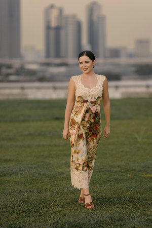 Beautiful Eastern European or Caucasian woman in a floral sand-colored dress posing against a modern city skyline with tall buildings and urban atmosphere. Stylish and graceful.の写真素材