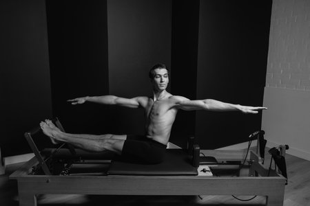 Slim male ballet dancer trains on Pilates equipment. Elegant pose, core strength, body controlの写真素材