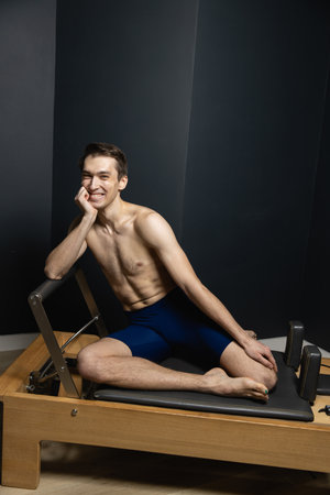 Slim male ballet dancer trains on Pilates equipment. Elegant pose, core strength, body controlの写真素材