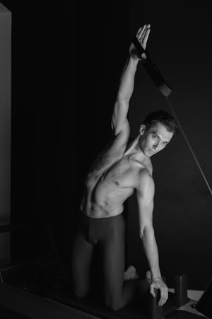 Slim male ballet dancer trains on Pilates equipment. Elegant pose, core strength, body controlの写真素材