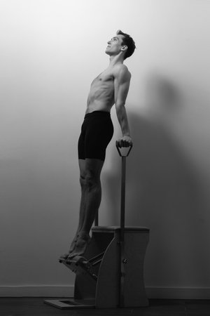 Slim male ballet dancer trains on Pilates equipment. Elegant pose, core strength, body controlの写真素材