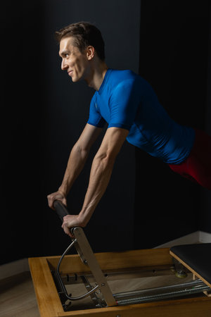 Slim male ballet dancer trains on Pilates equipment. Elegant pose, core strength, body controlの写真素材