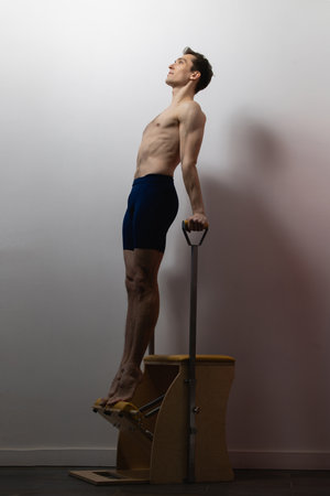 Slim male ballet dancer trains on Pilates equipment. Elegant pose, core strength, body controlの写真素材