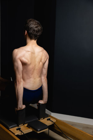 Slim male ballet dancer trains on Pilates equipment. Elegant pose, core strength, body controlの写真素材