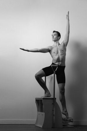 Slim male ballet dancer trains on Pilates equipment. Elegant pose, core strength, body controlの写真素材