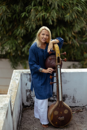 A fifty-year-old woman with blonde hair holds an Indian instrument called Sitarの写真素材