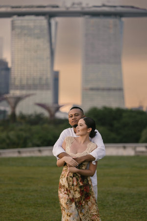 Close-up of an international couple embracing in front of Marina Bay Sands in Singapore. Asian man and Eastern European woman share a romantic moment outdoors, stylish and emotional atmosphere.の写真素材