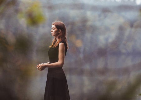 Young slim woman in black dress with beautiful nature background and soft bokeh effectの写真素材