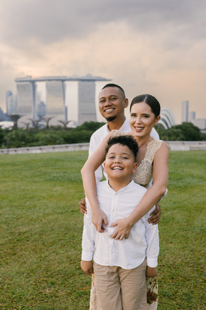 Happy mixed-race family with Asian father, Eastern European mother, and child smiling together near Marina Bay Sands in Singapore. Joyful outdoor moment in urban tropical city.の写真素材