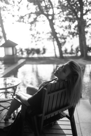 Elegant blonde woman in black robe relaxing on poolside lounger in luxury black and white photoの写真素材