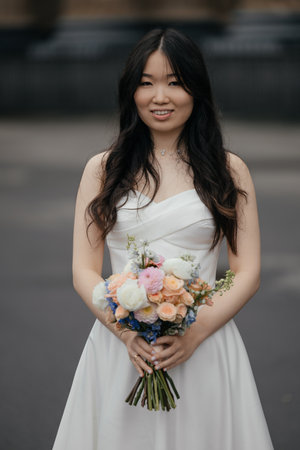 Beautiful Asian bride in wedding dress with bright bouquet in historic cityの写真素材