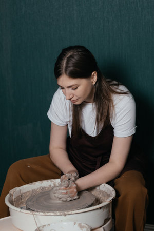 Young woman working with clay at pottery wheel in ceramic studio during creative processの写真素材