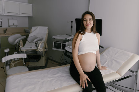 Portrait of beautiful pregnant Caucasian brunette with long hair in gynecology office