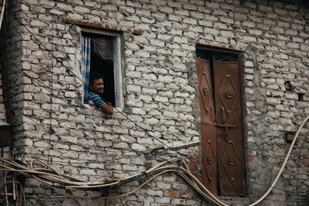 September 4, 2025 India: A man in the slums looking out of his window surrounded by urban decay.
