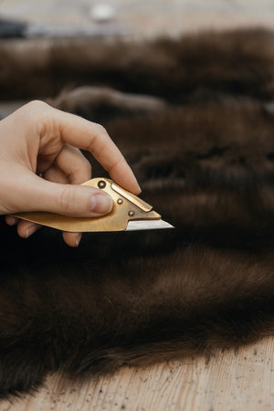 Close up of craftsman hand using furrier knife on natural pelt