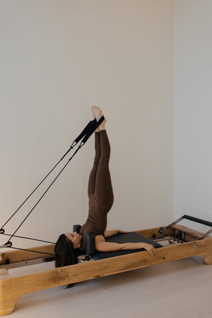Pilates Reformer machine with Pilates box attachment in use by a slim athletic model. She performs...