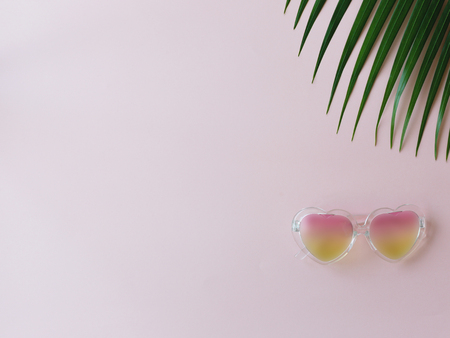 Heart-shape sunglasses and tropical leaf on the pink background. Minimal summer concept. Hipster vibes. Copy-space for your textの写真素材