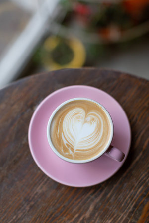 Beautiful pink cup of cappuccino on the wooden table background. Heart shape latte art, pastel pink ceramic cups.の写真素材