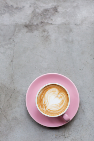 A beautiful pastel pink cup of cappuccino on the cement grunge background. Loft urban and hipster cafe concept. Trendy latte art.の写真素材