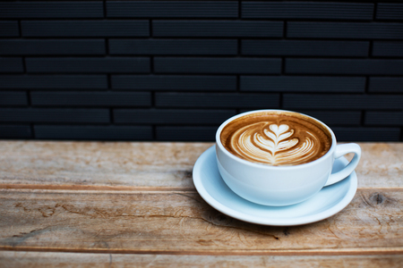 A beautiful cup of cappuccino with latte art in the wooden table and tile background. Trendy toning. Minimal composition, hipster vibes. Side view, copy space for your text.の写真素材