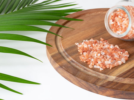 Beautiful pink Himalayan salt in the glass jar and white towel on the round wooden plank. Decorated...