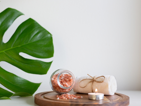 Beautiful pink Himalayan salt in the glass jar and white towel on the round wooden plank. Decorated by paml leaf. Relaxation and spa concept.の写真素材