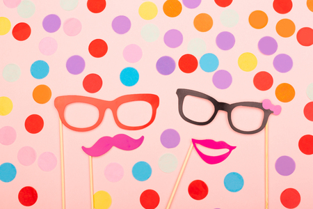 Male and female photo booth props on the pink background. Decorated wih multicolor confetti. Wedding, party or Birthday concept. Flat-lay, top view. Copy space for your text.の写真素材