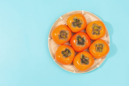 Beautiful persimmons in bamboo plate on the blue background. Autumn harvest. Asian vibes. Flat-lay,...