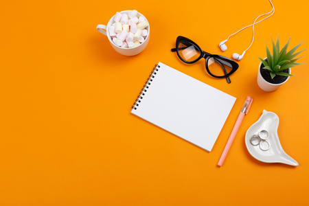 Creative feminine workplace with stationery supplies, eyeglasses and earphones. Cup with colorful marshmallows. Freelance, work at home or blogging concept. Bright colors. Copy space for your text.の写真素材
