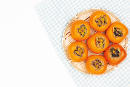 Beautiful persimmons on the piece of cloth. White background. Autumn harvest, Asian vibes. Flat-lay, top view, copy space.の写真素材
