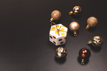 Christmas balls and a gift box on black background. Dark and moody still life composition. Flat-lay,...
