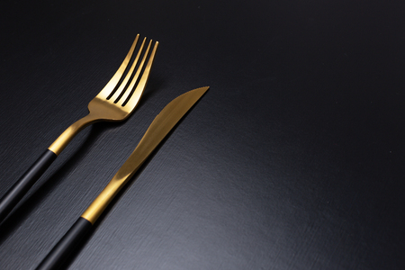 Set of stylish black and gold cutlery on black background. Dark and moody vibes. Fashionable and luxury eating. Flat-lay, top view. Copy space for your text.の写真素材