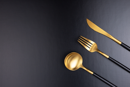 Set of stylish black and gold cutlery on black background. Dark and moody vibes. Fashionable and luxury eating. Flat-lay, top view. Copy space for your text.の写真素材