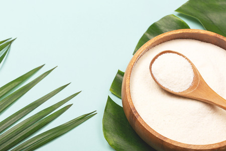 Collagen powder in bowl and measure spoon on palm leaf background. Extra protein intake. Natural beauty and health supplement. Minimal concept. Plant based collagen. Flatlay, top view. Copy space.の写真素材