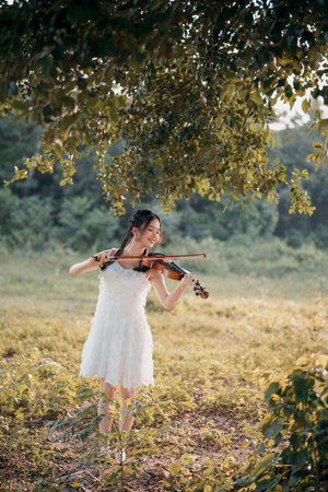 The girl is playing the violin under the big treeの写真素材