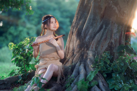 nostalgic theme, girl playing flute under treeの写真素材