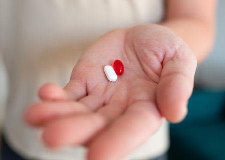 Close-up of a man's hand holding two pills red and whiteの写真素材