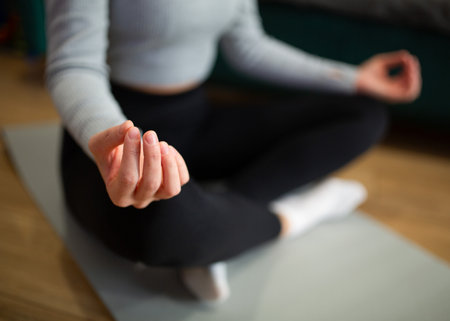 Close-up of woman meditating in lotus position at homeの写真素材
