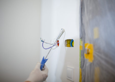 A person paints a wall in a room with a paint roller.