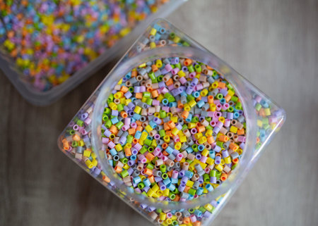 Colored beads in a glass container on a wooden background, top viewの写真素材