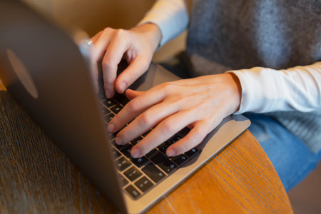 Close-up of woman hands typing on laptop keyboard at table in cafeの写真素材