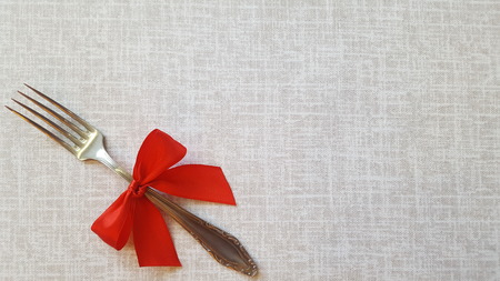 A fork with a red bow lies on the tablecloth. A place to record. Photo for the menu of cafe, restaurant, dining room, pizzeria. A place for a festive menu.の写真素材
