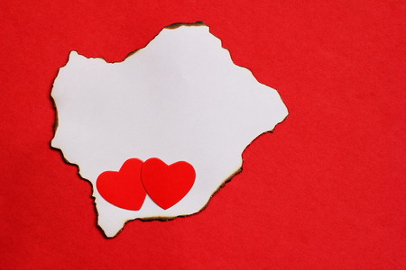 Two red hearts lie on a piece of white burnt paper. Red background. Empty space. concept of love.の写真素材